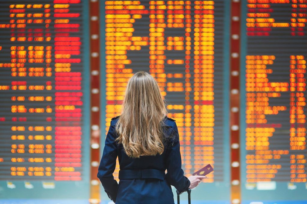 Young woman in international airport looking at the flight information board, checking her flight