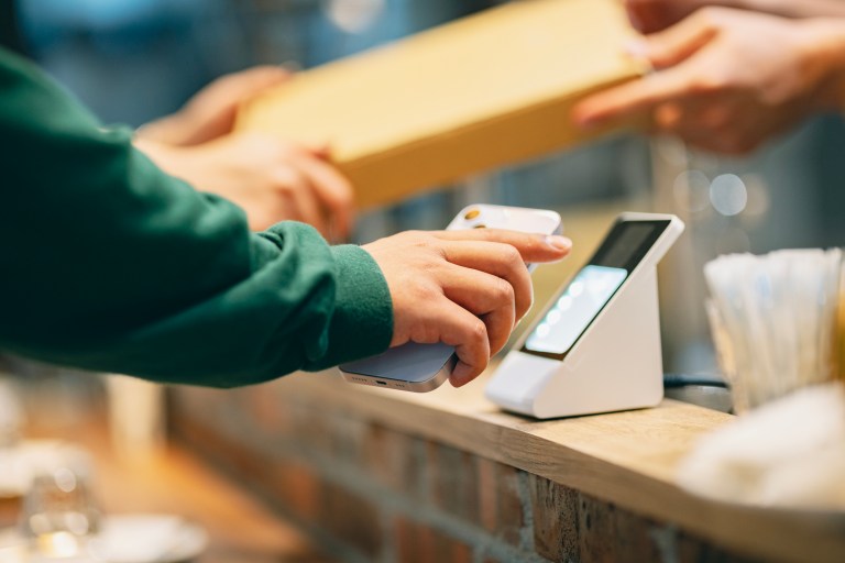 In the restaurant, a woman uses her smartphone to make a payment with the cashier. She scans the QR code using a card reader to complete a convenient contactless payment. At the same time, the cashier hands over the purchased pizza to the customer.